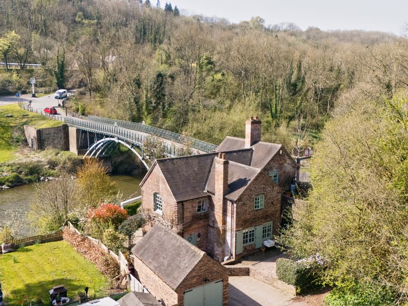 A drone view from April 2025 shows the toll cottage, the bridge and the wooded Gorge all at once, a perspective no historical photographer could have captured. It reveals the setting clearly: a crossing tucked tightly between steep wooded slopes, old riverside wharves and the winding Severn itself.