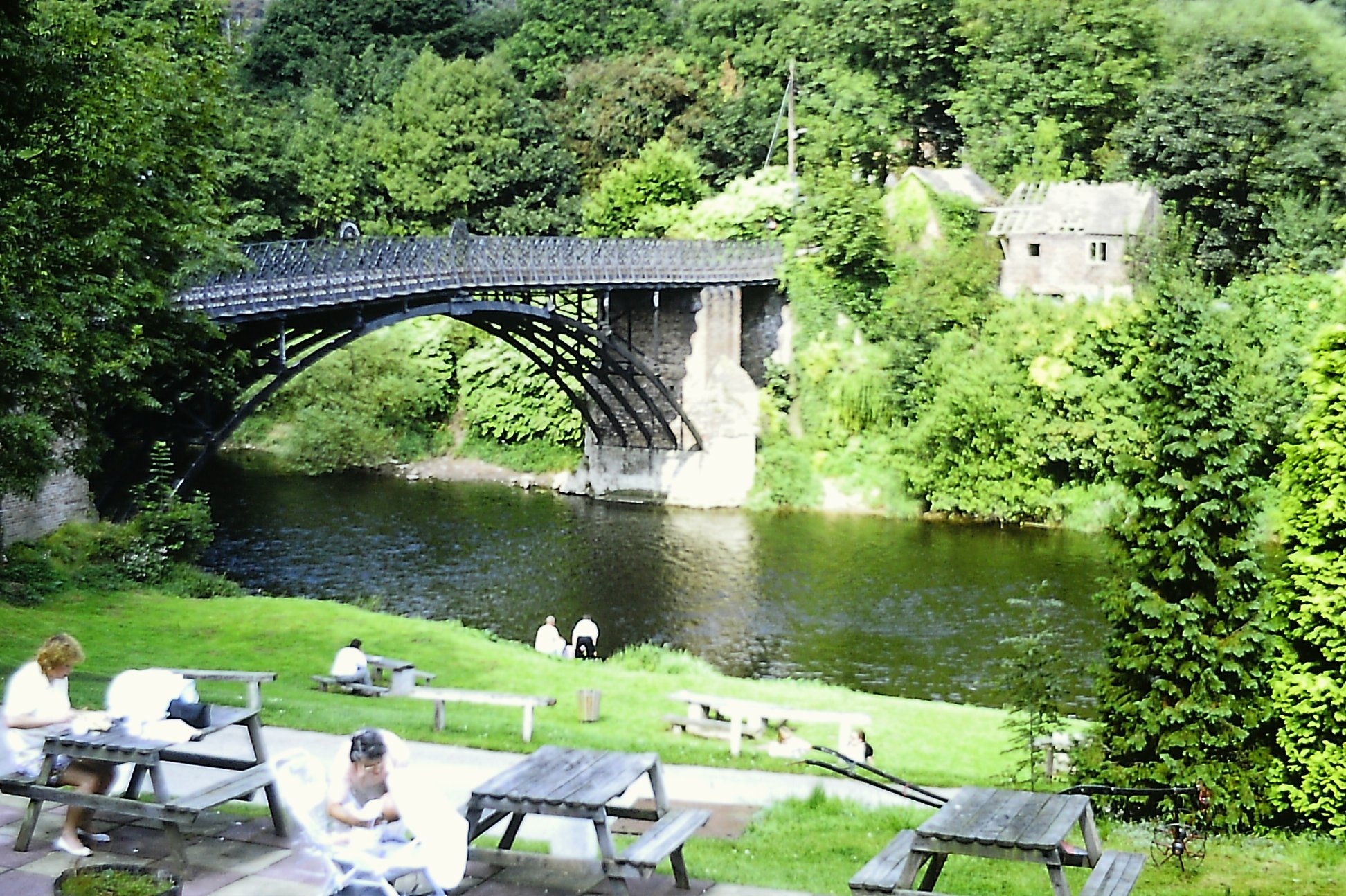 Picnic tables line the bank below the span today, walkers crossing the deck above, a scene of unhurried leisure that would have seemed odd to the tolls-paying traffic of earlier centuries. The Woodbridge Inn gardens beside the river remain the classic spot from which to view the arch in full.