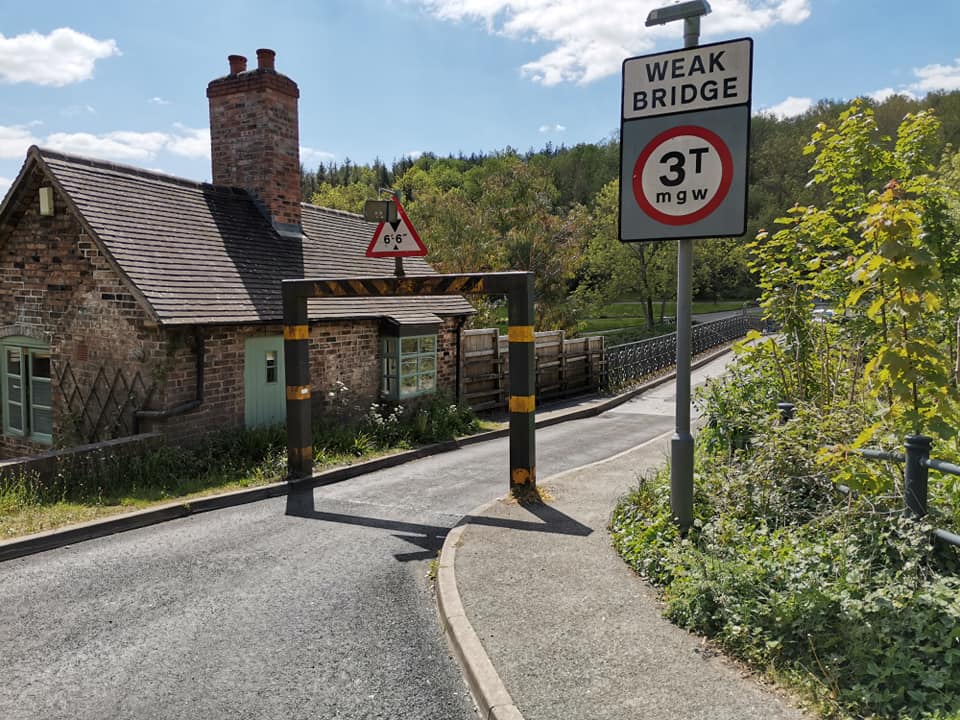 The bridge toll house today, framed by a modern 3T weak-bridge sign standing in front of it. It's a striking single view: two centuries of traffic control captured together, the eighteenth-century gatehouse and the twenty-first-century height barrier both doing essentially the same job of managing who gets across.