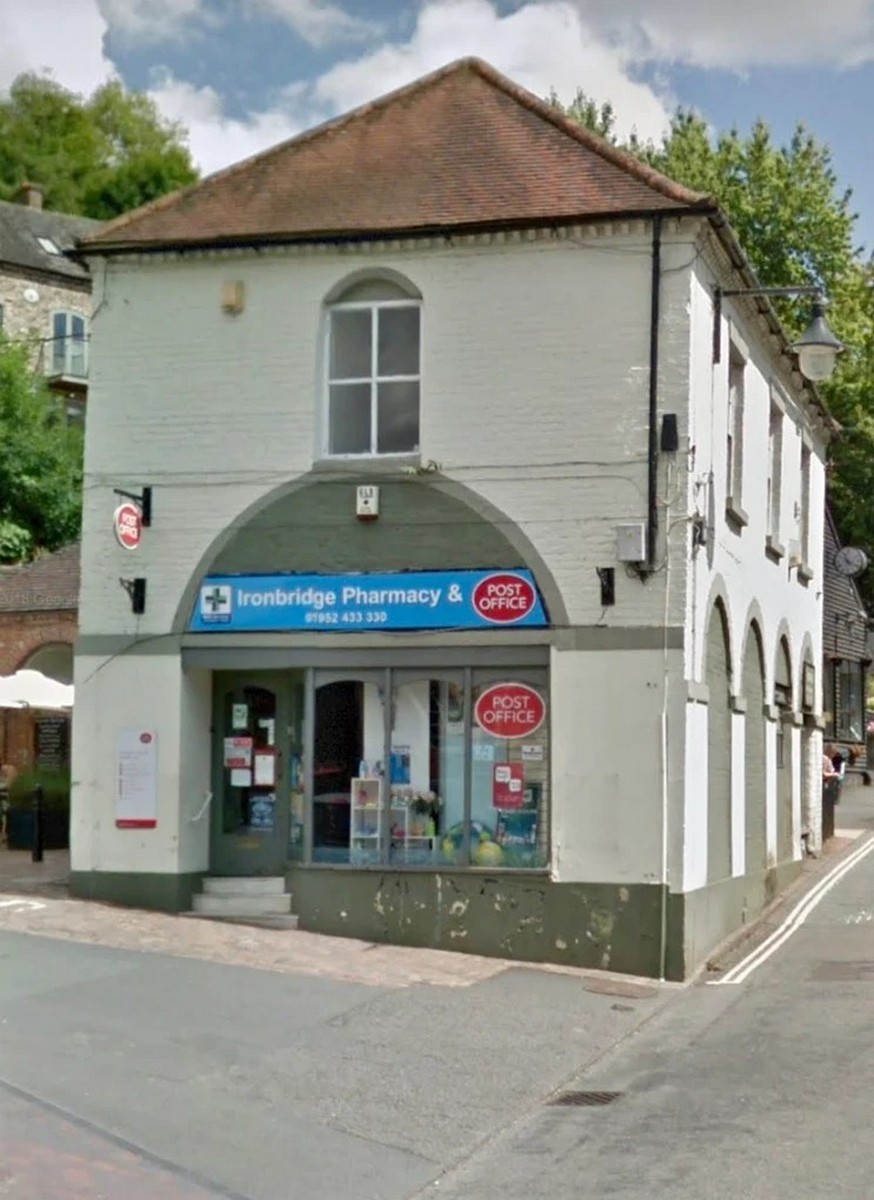 The same corner today, trading as Ironbridge Pharmacy & Post Office. Stand back and count the arches: the shape of the old market building is unchanged beneath the modern shopfront. Few buildings in the Gorge have carried on serving the town so continuously. Present day.