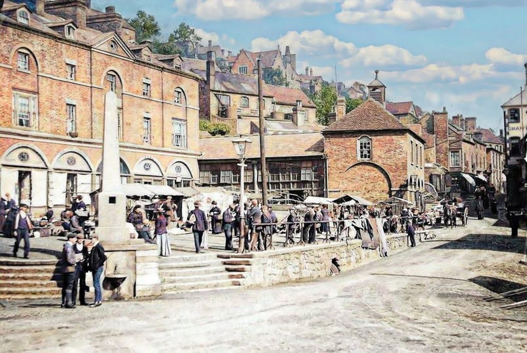 Stalls packed in below the fountain steps, canvas awnings pulled out over the goods. Notice how the traders have used the slope of the Square — the steps make a natural grandstand, and children always ended up sitting on them. Ironbridge held its market here for well over a century. Exact date unknown.