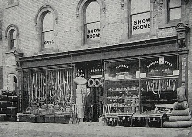 Historic photograph of the shop front, with signs for the OFFICE and SHOW ROOMS and advertising for Welsbach incandescent lighting.