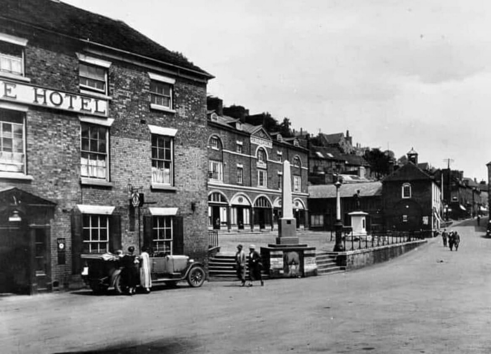 The obelisk standing above the Square with shops and awnings ranged behind it. Its height is deliberate: on market day you could find it over the heads of the crowd, which made it the obvious place to arrange to meet. Exact date unknown.