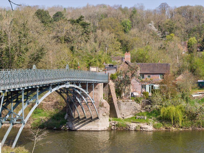 The green-painted span and its restored cottage, seen from the water in this recent photograph. It's easy to walk or drive past without registering the fact, but this is a Scheduled Ancient Monument still carrying everyday car traffic — a survival that is genuinely rare anywhere in Britain.