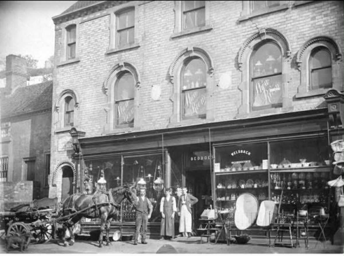 Historic photograph of the Beddoes shop frontage on High Street, with a horse and cart, people outside and goods displayed in front of the shop.